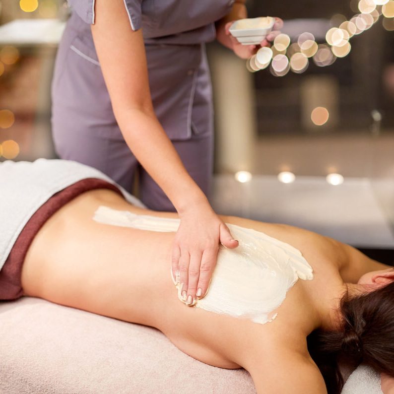people, beauty, healthy lifestyle and relaxation concept - beautiful young woman lying and having back massage with cream at spa